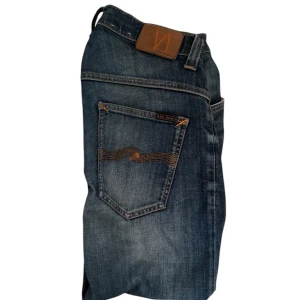 Nudie Jeans - Snygga blå jeans från Nudie Jeans med klassisk femficksdesign och kontrastsömmar på bakfickan. Jeansen har en cool tvättad look och är tillverkade i slitstarkt denim. Perfekta för dig som gillar en avslappnad och tidlös stil. defekt på bild 4 syns inte plus att du får oändligt med reperationer hos en nudie butik 😊