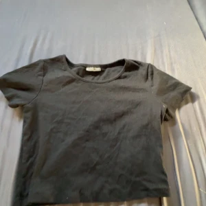 Svart croppad topp - En svart, enkel och croppad topp från Destiny. Modellen har rund halsringning och korta ärmar. Perfekt att matcha med jeans eller kjol för en clean look. Tunn och mjuk i materialet, passar dig som gillar basic men trendiga plagg.