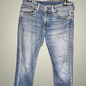 Levi's 511 blå jeans W34 L32 - Snygga Levi's 511 jeans i klassisk blå tvätt med lätt slitning. Modellen är slim och har fem fickor, dragkedjegylf och ikonisk läderpatch bak. Perfekta för dig som gillar en modern och stilren look. Materialet är tålig denim i bomull. Finns tyvärr en skada men det är bara att fringa mormor med symaskinen