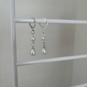 Silvriga örhängen med pärlor - Säljer ett par stilrena örhängen i silverfärg med hängande vita pärlor. Örhängena har både rund och droppformad pärla som ger en elegant look. Perfekta för att lyfta vilken outfit som helst. I rostfritt stål och handgjort 