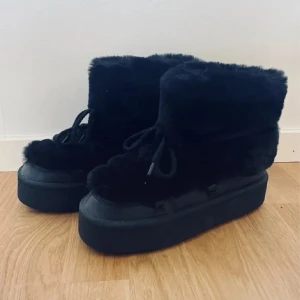 Svarta fluffiga boots med platå - Säljer ett par svarta moon boots med fluffigt pälsmaterial och grov platåsula. Skorna har snörning framtill och är perfekta för dig som vill ha en cool vinterlook. De är höga och riktigt mjuka, med rund tå och platt sula för extra komfort.