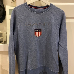 Blå sweatshirt från GANT  - Säljer en blå sweatshirt från GANT med broderad logga och sköld på bröstet. Storlek S. Väldigt bra skick. Köparen står för frakt!