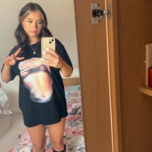 Svart oversized t-shirt med tryck - Cool svart oversized t-shirt med ett stort grafiskt tryck på framsidan som föreställer en mage och händer. T-shirten har korta ärmar och rund hals. Perfekt för dig som gillar statement-plagg och vill sticka ut med din stil.