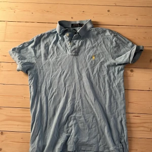 Ljusblå pikétröja från Ralph Lauren - Klassisk ljusblå pikétröja från Ralph Lauren med gul broderad logga på bröstet. Står att det är en M men passar även S