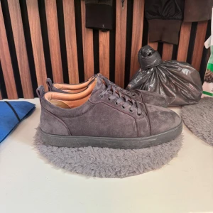 Christian Louboutin grå mockasneakers - Säljer ett par grå sneakers från Christian Louboutin i mocka med klassisk röd sula och snörning. Skorna har en stilren design med rund tå och svarta detaljer. Insidan är fodrad i ljusbrunt läder för extra komfort. Kommer med dustbag och äkthetskort. Tvättar innan jag skickar hör av er vid minsta fundering