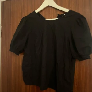 Svart puffärmad blus från Divided - Svart blus från Divided i storlek 36 med puffiga korta ärmar och rund halsringning. Tidlös och enkel design som passar till många olika stilar. Tillverkad i ett lätt tyg som känns skönt mot huden.