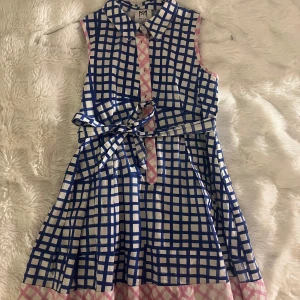 Rutig blåvit klänning från Milly - Superfin ärmlös klänning från Milly med blå och vita rutor, rosa detaljer och knappar framtill. Klänningen har krage och en lätt utställd kjol. Perfekt för dig som gillar färg och mönster!