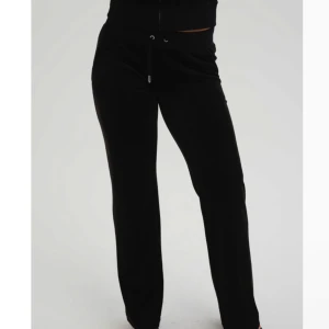 Svarta mjukisbyxor Juicy Couture XS - Svarta mjukisbyxor från Juicy Couture i supermjuk velour med utsvängda ben, snörning i midjan och bakfickor med silverfärgade knappar. Perfekta för en chill och trendig look.