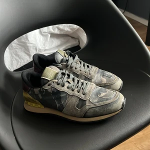 Camouflage sneakers från Valentino - Snygga sneakers från Valentino med ett coolt camouflage-mönster. Skorna har snörning och en unik design med detaljer i olika färger som grön, beige och vinröd. Perfekta för dig som vill ha en stilren men ändå iögonfallande look.