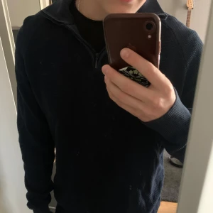 Mörkblå stickad tröja med half zip - Mörkblå stickad tröja med halv dragkedja i halsen. Tröjan har lång ärm och ribbade muddar vid ärmslut och nederkant. Perfekt för lager-på-lager och chill stil.