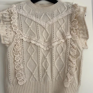 Stickad topp med spetsdetaljer från MNG - Supersöt stickad topp från MNG i ljusbeige med korta ärmar och dekorativa virkade spetsdetaljer. Snyggt kabelstickat mönster och ribbad nederkant. Perfekt för dig som gillar romantisk och unik stil.