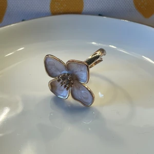 Guldig ring med stor blomma - Unik ring i guldton med en stor, vitblommig detalj framtill. Blomman har fyra kronblad med marmorerad yta och guldfärgade kanter samt små guldfärgade prickar i mitten. Perfekt statement-piece för dig som vill sticka ut.