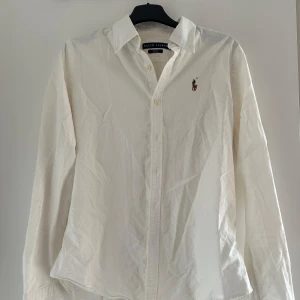Vit slim fit skjorta från Ralph Lauren - Vit skjorta från Ralph Lauren i slim fit-modell med klassisk krage och knappar framtill. Långärmad och tillverkad i mjuk bomull. 