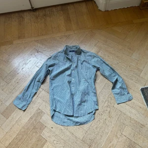 Rutig skjorta från Ralph Lauren - Snygg rutig skjorta från Ralph Lauren i grönt, blått och vitt. Klassisk krage, knäppning framtill och lång ärm. Broderad logga på bröstet. Perfekt för dig som gillar preppy stil och vill ha något som sticker ut lite extra.