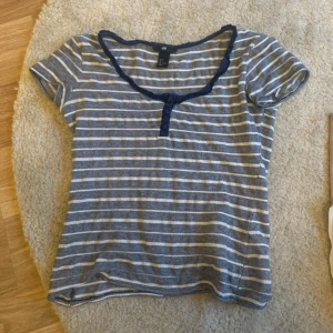 Randig babydolltopp i blått och vitt - Säljer en randig topp från H&M i blått och vitt med rundad halsringning och knappdetalj framtill. Toppen har korta ärmar och är tillverkad i mjuk bomull, perfekt för en avslappnad stil.