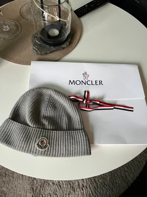 Grå moncler mössa - Säljer monclermössa från deras egna hemsida, köpt i februari 2025 och har använts ibland, då o då, orginalförpackningen finns plus kvitto i telefonen som kan bevisas, pris kan sänkas, vill ha bort så snabbt som möjligt!