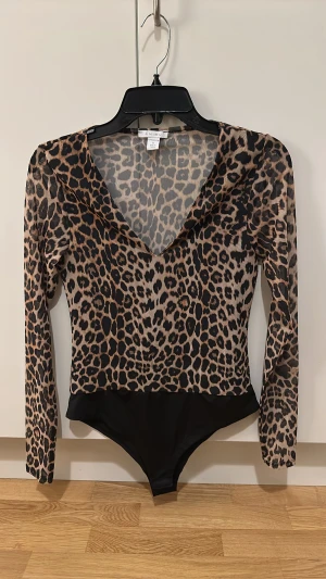 Leopardmönstrad mesh bodysuit från Amisu - Säljer en snygg leopardmönstrad bodysuit från Amisu i storlek S. Toppen har lång ärm, djup v-ringning och är gjord i tunn mesh med svart botten. Perfekt för dig som vill sticka ut med ett djuriskt print och cool siluett.