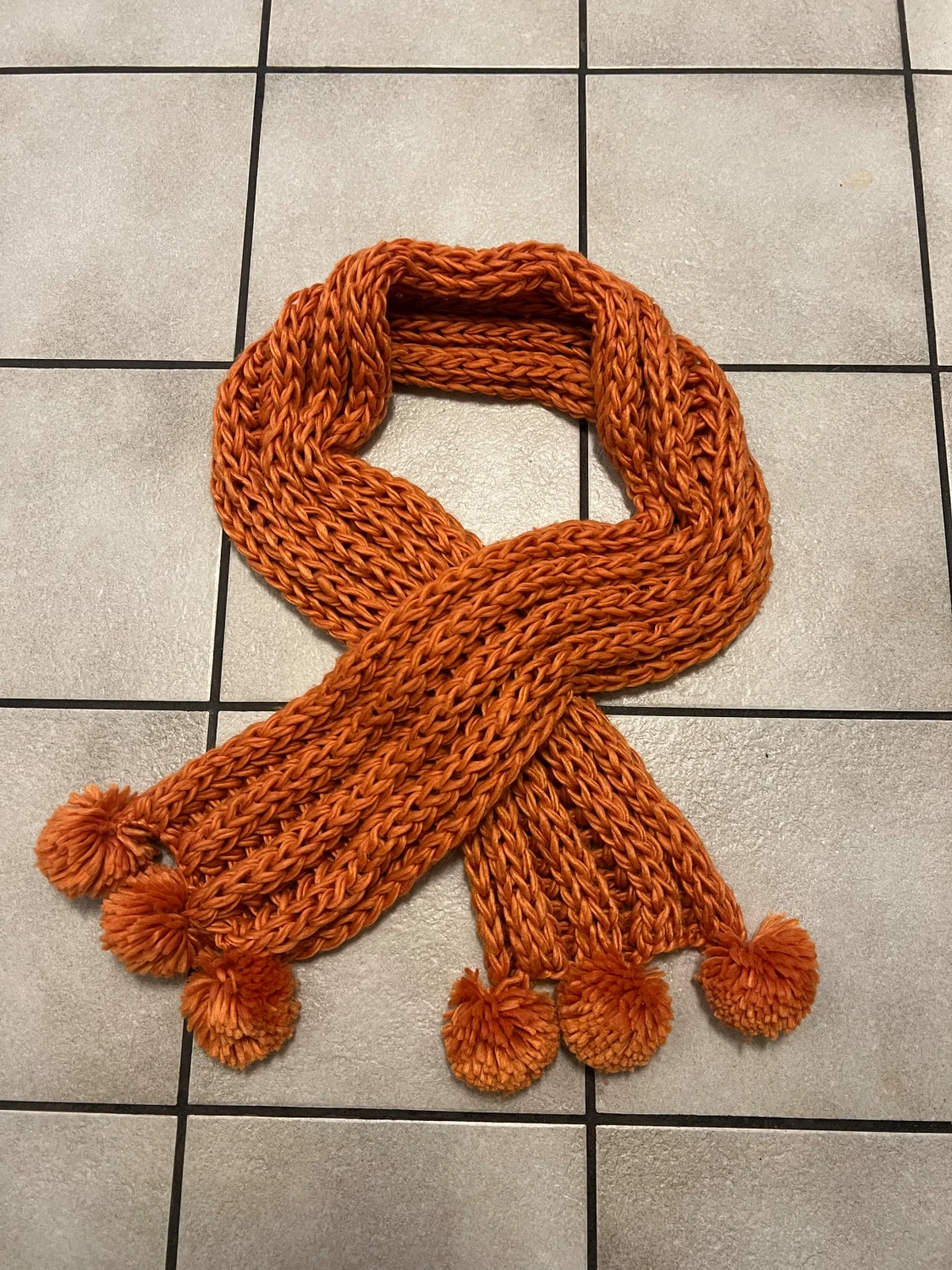 Orange stickad halsduk med tofsar