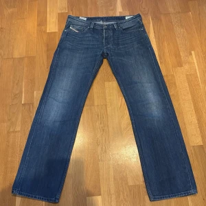 Blå Diesel Larkee jeans W33 L32 - Säljer ett par klassiska blå Diesel Larkee jeans med raka ben och normal passform. Jeansen har snygga slitningar, fem fickor och detaljerade sömmar. Perfekta för dig som gillar en avslappnad stil med lite bredare ben. Materialet är robust denim.