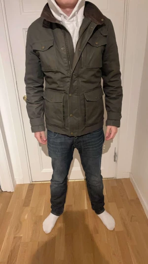 Bondelid overshirt  - Snygg mörkgrön parkajacka med klassisk krage och flera praktiska fickor framtill. Jackan har knappar och dragkedja, samt detaljer med knappar baktill i midjan. Perfekt för dig som gillar en stilren och funktionell look.