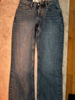 Blå raka jeans från 157 Icon, S - Säljer ett par klassiska blå jeans från 157 Icon i storlek S. Jeansen har lågmidja, raka ben och femficksmodell med knappgylf. Perfekta till en avslappnad look. Helt oanvända!