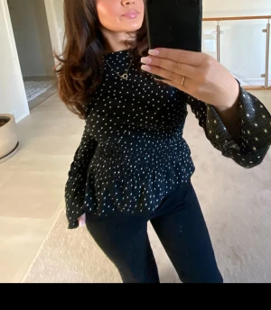 Prickig smock topp från Gina - Säljer en svart blus med vita prickar och volangärmar. Blusen har smockad midja som ger en snygg form