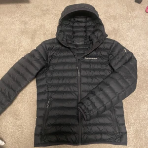 Svart dunjacka Peak Performance - Säljer en svart dunjacka från Peak Performance med huva och dragkedja framtill. Den är använd max 10 gånger och är i grymt skick! Hör av er vid frågor eller funderingar.