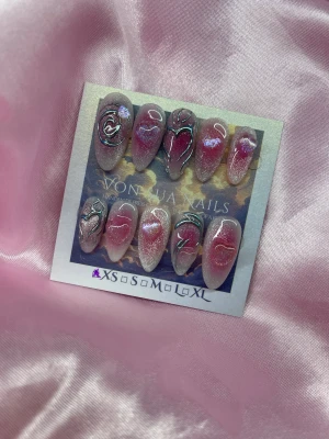 GlitteryHearts (XS);Medium Almond - Set med handgjorda press-on naglar i rosa och silverglittrigcateye , korean blush med charms i form av hjärtan och 3D nailart i swirl-mönster. Naglarna har en medium almondform och skimrande finish med holografiska detaljer. Perfekt för dig som vill ha unika och kreativa naglar.XS: 14 mm, 11 mm, 11,5 mm, 10 mm, 8 mm 