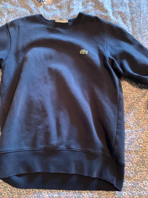 Marinblå sweatshirt från Lacoste - Snygg marinblå sweatshirt från Lacoste med klassisk rund hals och det ikoniska krokodilmärket broderat på bröstet. Tröjan har långa ärmar och är gjord i mjuk bomull, perfekt för chill dagar. Enkel och stilren design som funkar till allt.