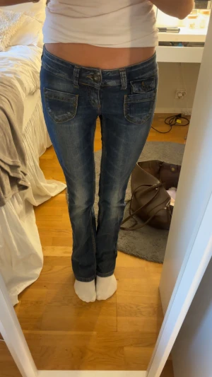 Blå bootcut jeans med låg midja - Snygga blå jeans med bootcut och låg midja, klassisk femficksdesign och slitna detaljer. Jeansen har markerade sömmar och är tillverkade i jeansmaterial med en cool tvättad look. Perfekt för dig som gillar retrovibbar och vill ha en avslappnad stil. Stl 27/32, använda men i fint skick 