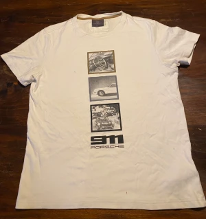 Vit Porsche 911 t-shirt med tryck - Vit t-shirt från Porsches limiterade kollektion med coolt tryck på framsidan som visar klassiska 911-bilder. Baksidan har ett diskret 60-årsjubileumstryck med årtalen 1963-2023. T-shirten är i mjuk bomull och har rund hals och korta ärmar. Perfekt för dig som älskar bilar och stil. (Pris går att diskutera vid smidig affär)