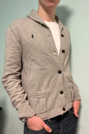 Ralph Lauren Cardigan - Säljer denna stilrena och snygga gråa cardigan från Ralph Lauren. Plagget är i mycket bra skick och passar perfekt både till vardags och när du vill klä upp dig.  Har du några frågor? Tveka inte att höra av dig. Allt gott från Deluxe garderoben ⭐️ 