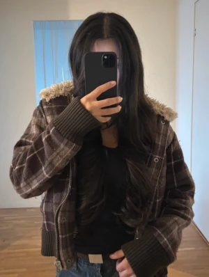 Vinterjacka y2k - Mysig brun teddyjacka från Dcate med rutigt mönster, fluffigt foder och huva. Jackan har dragkedja, ribbade muddar och två fickor framtill. Perfekt för kalla dagar när du vill vara både varm och snygg.