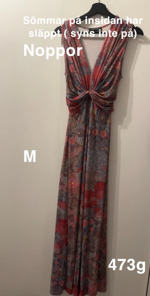 Mönstrad långklänning med knut - Färgstark långklänning från ilse Jacobsen med paisleymönster i rosa, blått och beige. Djup v-ringning och snygg knutdetalj framtill. Ärmlös modell i mjukt, stretchigt material som faller fint. Perfekt för dig som gillar bohemisk och unik stil.🌸 Så mjuk och skön. Har släppt på sömmarna vid brösten Finns noppor. Storlek M