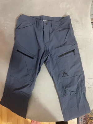 Mörkblå cargopants från McKinley - Snygga mörkblå cargopants från McKinley med praktiska dragkedjefickor på benen och klassisk knappstängning i midjan. Byxorna har en loose passform och är tillverkade i slitstark. 