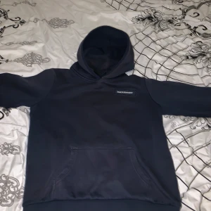 Mörkblå hoodie från Peak Performance - Snygg mörkblå hoodie från Peak Performance med broderad logga på bröstet. Klassisk modell med huva och stor känguruficka framtill. Mjuk och skön bomullsblandning, perfekt för chill dagar eller när du vill ha en clean look.