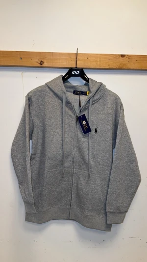 Grå zip hoodie - Säljer en stilren grå hoodie med dragkedja och snörning i huvan. Tröjan är tillverkad i mjuk bomull. Perfekt för chill dagar och enkel att matcha med jeans eller joggers.