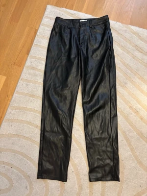 Svarta skinnbyxor från NLY Trend - Snygga svarta skinnbyxor från NLY Trend i storlek 36. Byxorna har klassisk femficksdesign, bälteshällor och dragkedja med knapp framtill. Materialet är syntetiskt skinn som ger en cool och edgy vibe. Passformen är rak och midjan är normal.