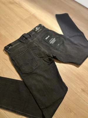 Replay Anbass slim fit jeans mörkgrå - Snygga Replay Anbass jeans i slim fit med mörkgrå tvätt. Klassisk femficksdesign, raka ben och diskreta sömmar. Jeansen är tillverkade i mjukt denim-material med stretch för extra komfort. Perfekt för dig som gillar stilrena och moderna jeans.