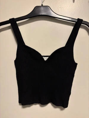 Svart ribbad linnetopp från H&M - Säljer en svart ribbad linnetopp från H&M med breda axelband och en snygg v-ringad skärning framtill. Toppen är croppad och har en stilren, enkel design som är lätt att matcha. Perfekt för dig som gillar minimalistisk stil.