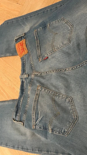 Levi's 514 blå jeans W32 L34 - Säljer ett par klassiska Levi's 514 jeans i ljusblå tvätt. Modellen har raka ben, fem fickor och snygga kontrastsömmar. Tillverkade i slitstarkt bomullsjeansmaterial och har Water<Less-teknologi för mindre vattenförbrukning. Perfekta för en avslappnad look.