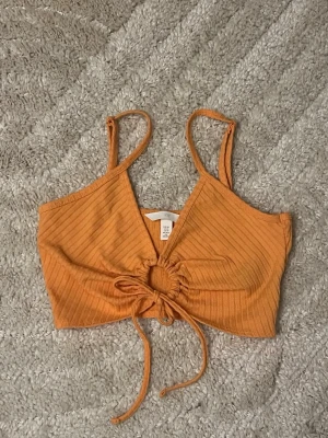 Orange ribbad croppad linnetopp H&M XS - Säljer en orange croppad linnetopp från H&M i storlek XS. Toppen har ribbad struktur, smala axelband och snygg snörning framtill med en rund detalj. Använd max 1-2 gånger. Fint skick! 