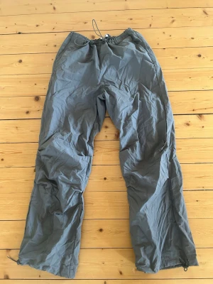 Byxor  - Grå byxor med fickor på baksidan och går att spänna åt både i midjan och vid benen 