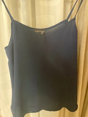 Mörkblå linnetopp  - Säljer en stilren mörkblå linnetopp från Topshop med smala axelband och enkel design. Toppen är ärmlös och har en mjuk, slät yta i syntetmaterial. använt några gånger