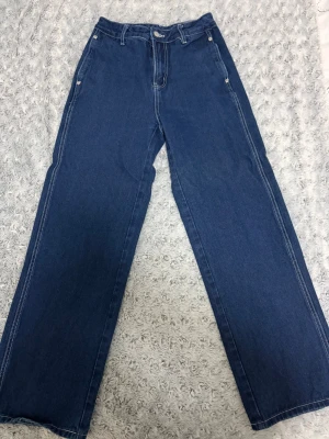 Blå wide jeans med snörning - Säljer ett par blå jeans med breda ben och kontrastsömmar. Modellen har hög midja, klassisk knappstängning och stora bakfickor. Ett par har snörning i midjan och resår vid benslut för en chill vibe. Perfekt för dig som gillar loose fit och streetstyle. Har aldrig använt dom första paret är storlek S och andra är STORLEK XS säljer båda tillsammans för 200kr