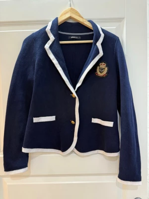 Mörkblå stickad kavaj från Gina Tricot - Snygg mörkblå stickad kavaj med vita kanter och guldknappar från Gina Tricot. Klassisk krage och långärmad modell.