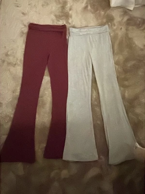 Två par bootcut yoga pants byxor, vinröd & ljusgrå - Säljer två par bootcut yoga pants byxor, ett par i vinröd och ett par i ljusgrå färg. Båda har hög midja och är gjorda i mjukt stretchigt tyg, perfekta för en chill och snygg look. Passar dig som gillar bekväma och trendiga byxor med lite utsvängda ben. Kontakta mig om ni bara är intresserade av ett par😊