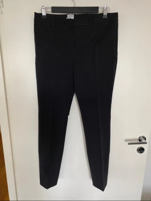 Svarta kostymbyxor från Filippa K - Snygga svarta kostymbyxor från Filippa K i klassisk rak modell. Byxorna har bälteshällor, diskreta sidofickor och är tillverkade i ett mjukt material som ger en stilren look. Perfekta för dig som gillar minimalistisk design och vill ha ett par byxor som funkar till många olika stilar.