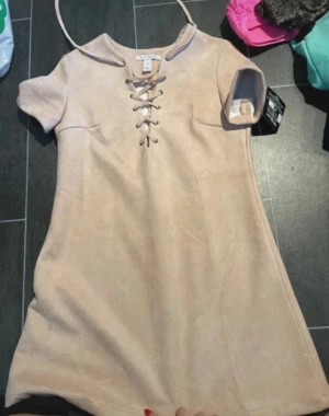 Beige kortklänning med snörning - Supersnygg beige kortklänning från Salt Tree i mockaimitation. Klänningen har korta ärmar och cool snörning framtill vid halsen som ger en trendig touch. Perfekt för dig som gillar stilrena och enkla plagg med en twist.