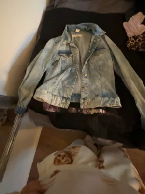 Ljusblå jeansjacka Label of Graded Goods - Säljer en klassisk ljusblå jeansjacka från Label of Graded Goods i storlek 36. Jackan har knappar framtill, två bröstfickor med lock och en snygg krage. Perfekt att slänga över en hoodie eller t-shirt för en chill look.